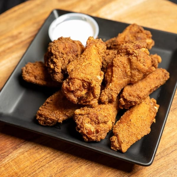 Crispy fried chicken wings with a side of ranch dressing on a black plate.